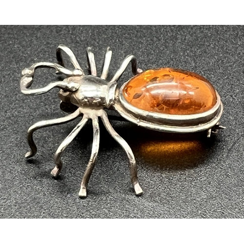 1047 - A silver and amber spider shaped brooch set with an oval amber cabochon. Silver mark to underside. A... 