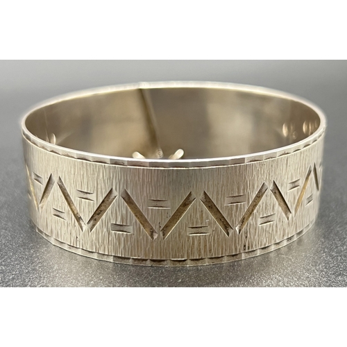 1048 - A vintage 2cm wide Zeeta silver bangle with Aztec style decoration, diagonal sliding clasp and safet... 