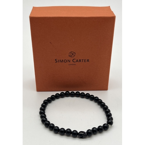 1073 - A black onyx round bead stretch bracelet with single skull shaped bead by Simon Carter, London. New ... 