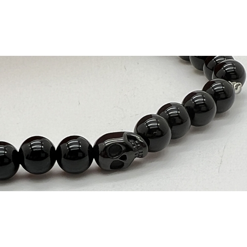 1073 - A black onyx round bead stretch bracelet with single skull shaped bead by Simon Carter, London. New ... 