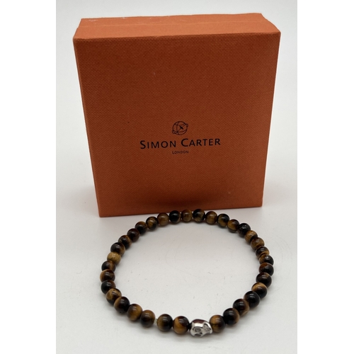 1074 - A men's tigers eye bead stretch bracelet with silver tone skull shaped bead by Simon Carter, London.... 