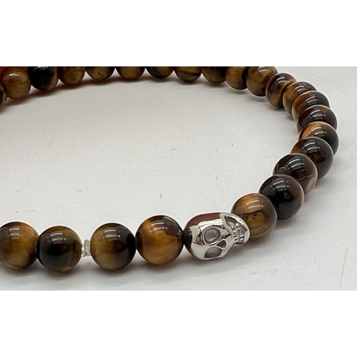 1074 - A men's tigers eye bead stretch bracelet with silver tone skull shaped bead by Simon Carter, London.... 