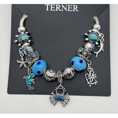 1077 - A costume jewellery charm bracelet with multiple charms by Bijoux Terner, new and with packaging. Ch... 