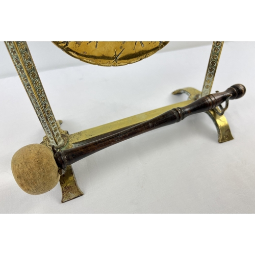 1194 - An antique brass freestanding dinner gong with turned wooden handled beater. Approx. 33.5cm tall.