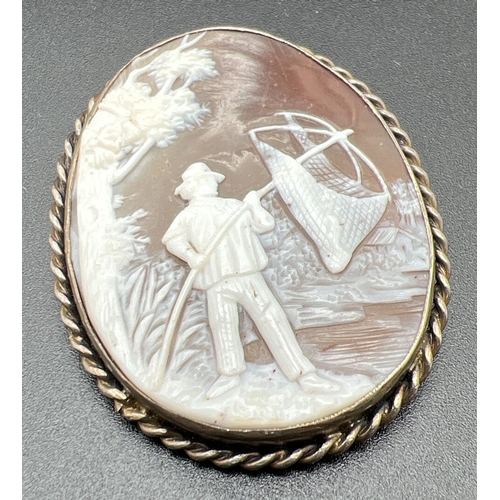 A vintage white metal oval cameo brooch with gentleman fishing scene. Rope design to brooch mount. Approx. 4.4cm x 3.5cm.
