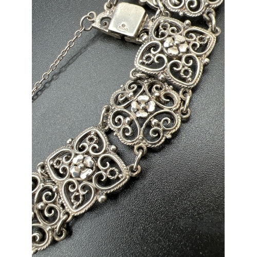 1035 - A decorative floral and scroll pierced work 10 panel bracelet with push clasp and safety chain. Silv... 