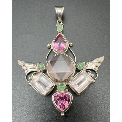 A large handmade "The Rose trinity" gemstone set large self healing winged pendant by Shankari the Alchemist. Set with 4 oval cut white opals, a pear cut and a trillion cut pink topaz, 2 emerald cut rose quartz stones and a large central round cut rose quartz stone. The 5 larger stones set in scroll work mounts. Silver mark to back of bale. Hand signed to back of pendant. Approx. 8cm x 7cm.