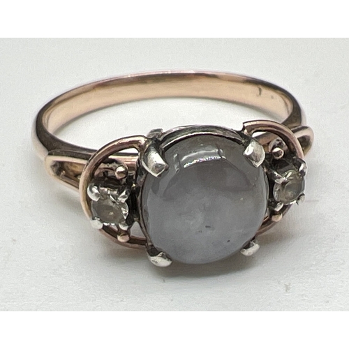 An antique Arts & Crafts grey moonstone and clear quartz 9ct rose gold dress ring. Central round grey moonstone cabochon with a small round cut clear quartz stone either side. Very worn mark to inside of band. Tests as 9ct gold. Total weight approx. 4g. Ring size P.