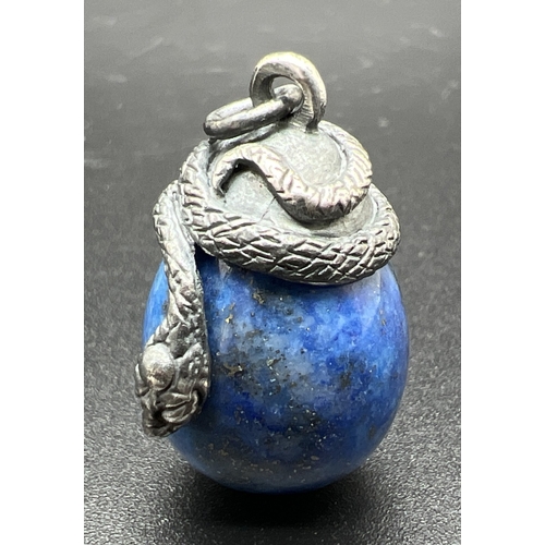 1065 - A pendant modelled as a white metal snake coiled over an egg shaped piece of lapis lazuli. Total len... 