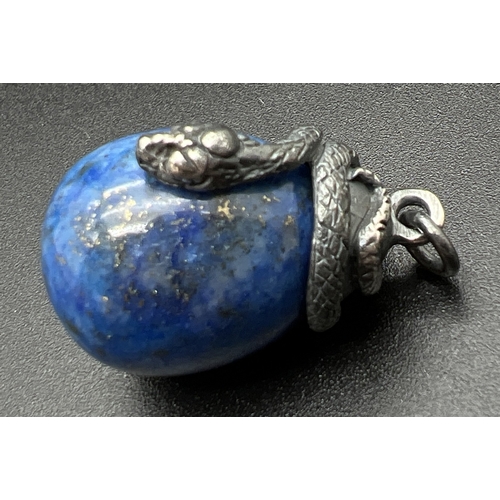 1065 - A pendant modelled as a white metal snake coiled over an egg shaped piece of lapis lazuli. Total len... 