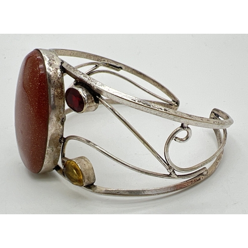 1098 - A silver modern design open scroll work cuff bangle set with large central brown sandstone, 2 oval c... 