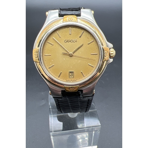 A men's 9040M wristwatch by Gucci with replacement black leather strap. Gold tone and stainless steel case with brushed gold face and bold gold hour markers and hands. Date function and seconds hand. Gucci logo to case, winder and back. Working order.