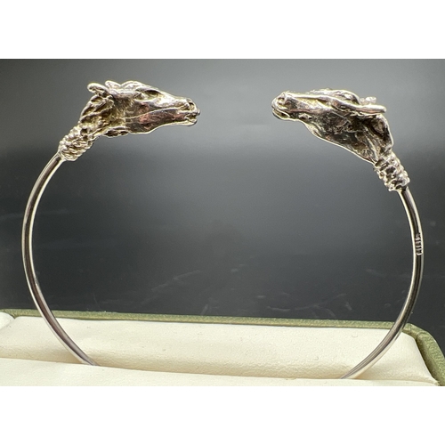4 - A 900 silver thin cuff style bangle with double horse head detail. Silver mark on edge of bangle.