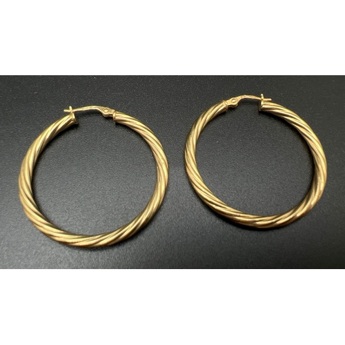 7 - A pair of 9ct gold twist design hoop earrings. Gold marks on hinged posts. Approx. 3.5cm diameter. T... 