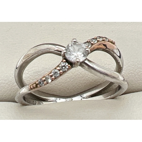 72 - A silver stone set Clogau ring in a crossover design, with rose gold accents. Central round cut clea... 