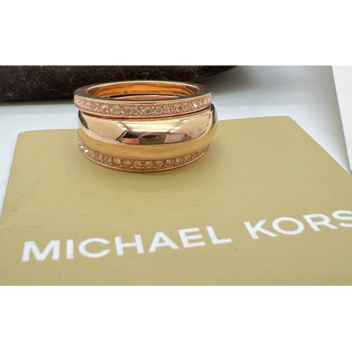 80 - 2 items of Michael Kors jewellery. A gold tone stone set double intertwined band ring set with clear... 