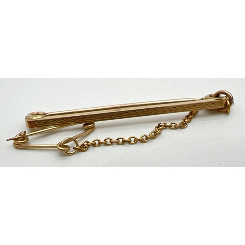 87 - A 9ct gold tie pin with safety chain and engine turned decoration. Gold marks to back. Total weight ... 