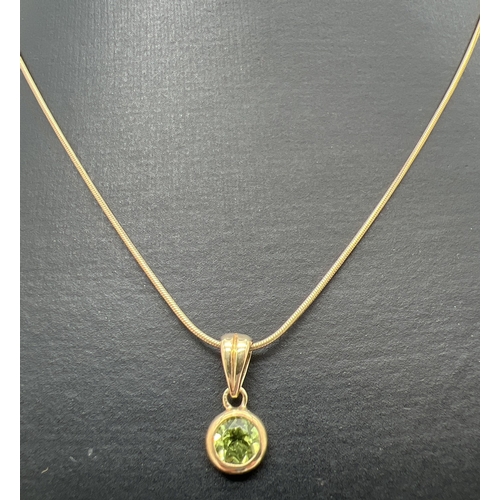 104 - A modern design 9ct gold and peridot pendant necklace. A bezel set round cut peridot drop pendant on... 