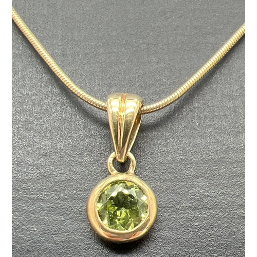 104 - A modern design 9ct gold and peridot pendant necklace. A bezel set round cut peridot drop pendant on... 