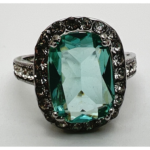 130 - A large silver stone set cocktail ring. Central emerald cut pale green stone surrounded by 22 round ... 