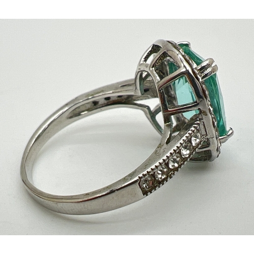 130 - A large silver stone set cocktail ring. Central emerald cut pale green stone surrounded by 22 round ... 