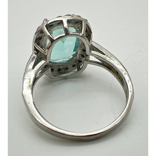 130 - A large silver stone set cocktail ring. Central emerald cut pale green stone surrounded by 22 round ... 