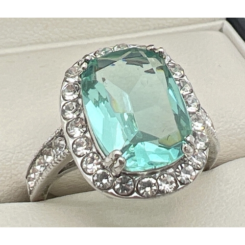 130 - A large silver stone set cocktail ring. Central emerald cut pale green stone surrounded by 22 round ... 