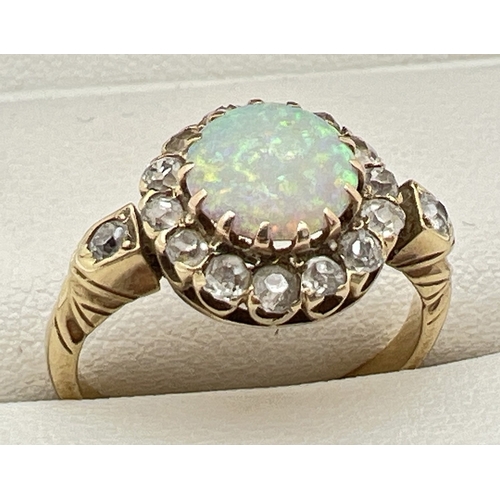 An unmarked yellow gold halo style opal and diamond dress ring. Central round cut opal surrounded by 14 round cut diamonds with a single round cut diamond to each shoulder. Ring size L. Total diamond approx. 0.30ct. Opal approx. 6mm diameter. Tests as 18ct gold. Total weight approx. 3.4g