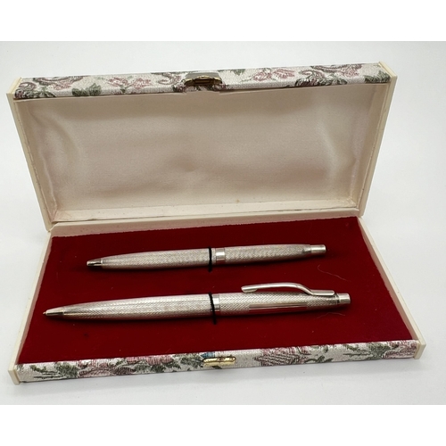 1202 - A boxed set of 2 vintage silver writing pens, both ball point. Engine turned decoration to both with... 