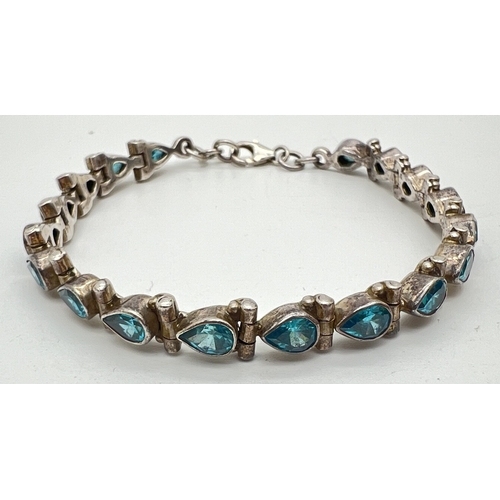 1040 - A silver and bright blue apatite gemstone set tennis style bracelet with lobster claw clasp. 18 tear... 