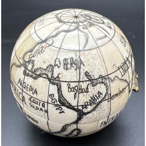 1305 - A Scrimshaw style carved globe with inset compass to interior. Possibly bone, approx. 7cm diameter.