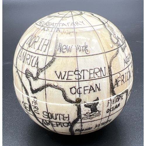 1305 - A Scrimshaw style carved globe with inset compass to interior. Possibly bone, approx. 7cm diameter.