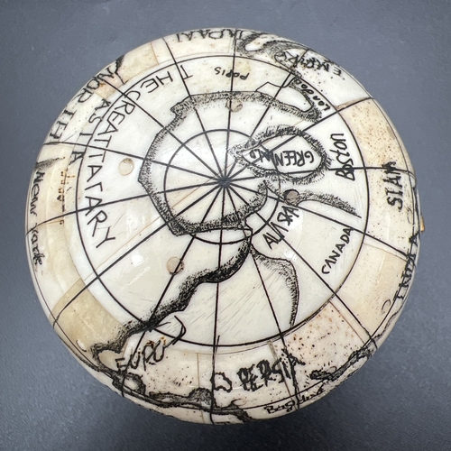 1305 - A Scrimshaw style carved globe with inset compass to interior. Possibly bone, approx. 7cm diameter.