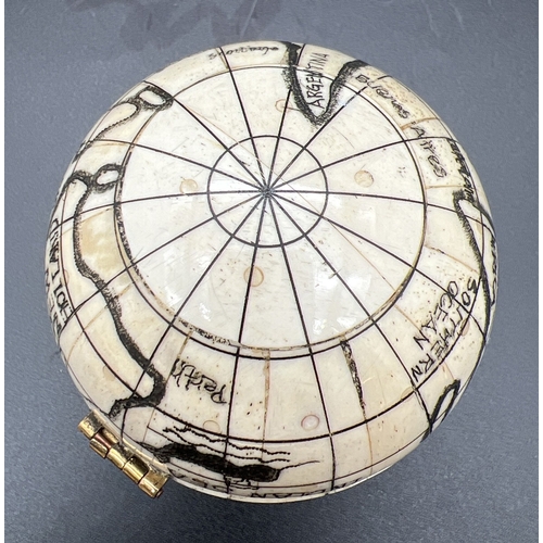 1305 - A Scrimshaw style carved globe with inset compass to interior. Possibly bone, approx. 7cm diameter.