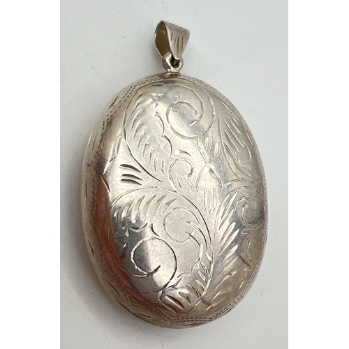 1021 - A large silver oval shaped locket with engraved foliate & scroll design front and back. Silver mark ... 