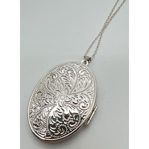 1052 - A large silver oval shaped locket engraved with scroll & foliate design to each side, on a 26 