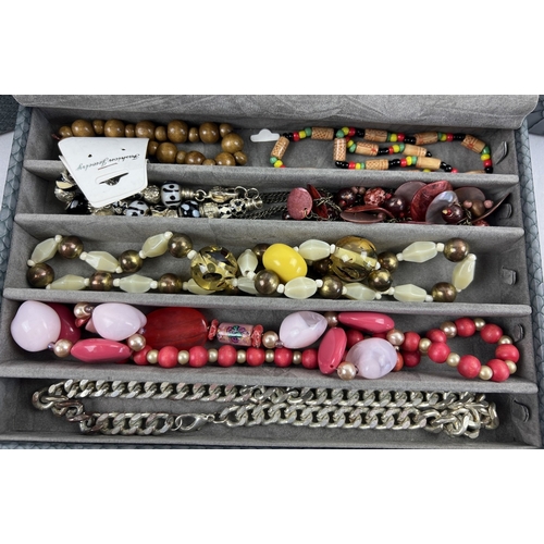 1059 - A modern faux snake skin stacking jewellery box containing a quantity of assorted costume jewellery.... 