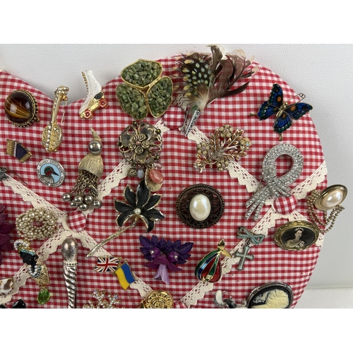 1061 - A padded heart shaped pin board containing approx. 60 assorted vintage brooches. To include enamelle... 