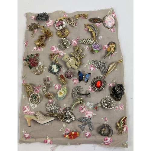 1063 - A padded fabric panel containing approx. 45 assorted vintage brooches. To include wooden, gold tone,... 