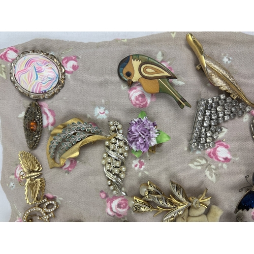 1063 - A padded fabric panel containing approx. 45 assorted vintage brooches. To include wooden, gold tone,... 