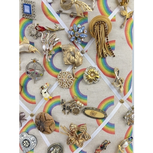 1060 - A padded pin board containing approx. 82 assorted vintage brooches. To include gold tone, stick pin,... 