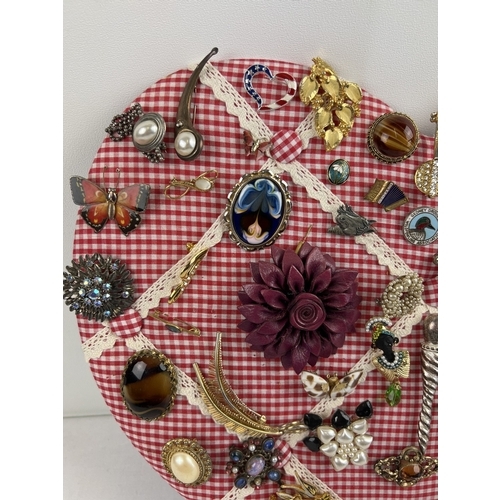 1061 - A padded heart shaped pin board containing approx. 60 assorted vintage brooches. To include enamelle... 