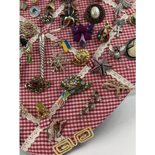 1061 - A padded heart shaped pin board containing approx. 60 assorted vintage brooches. To include enamelle... 