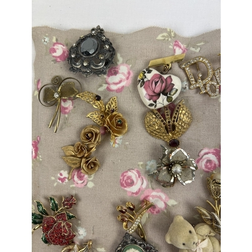 1063 - A padded fabric panel containing approx. 45 assorted vintage brooches. To include wooden, gold tone,... 