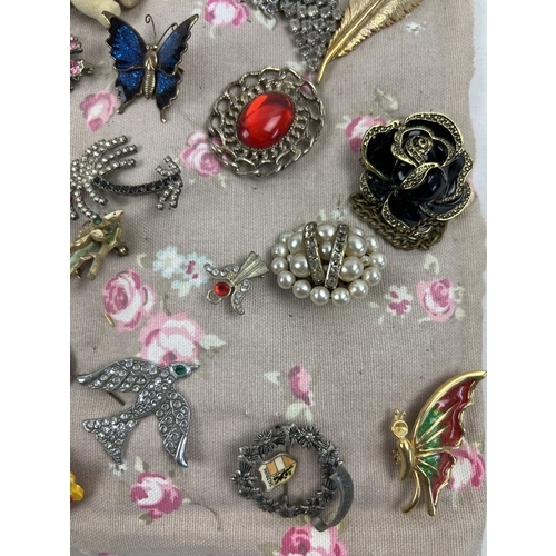 1063 - A padded fabric panel containing approx. 45 assorted vintage brooches. To include wooden, gold tone,... 