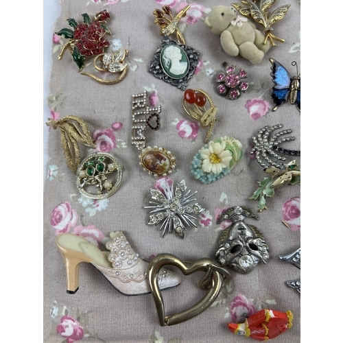 1063 - A padded fabric panel containing approx. 45 assorted vintage brooches. To include wooden, gold tone,... 