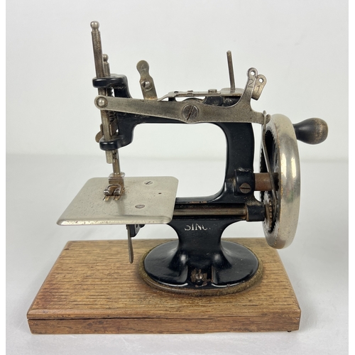 140 - An antique black cast iron toy Singer sewing machine, on a wooden base. Approx. 21cm tall.