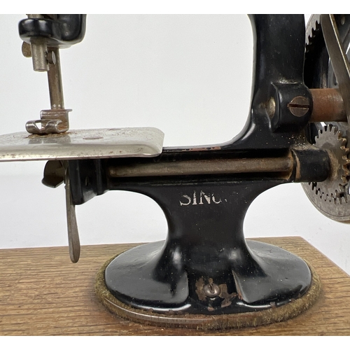 140 - An antique black cast iron toy Singer sewing machine, on a wooden base. Approx. 21cm tall.