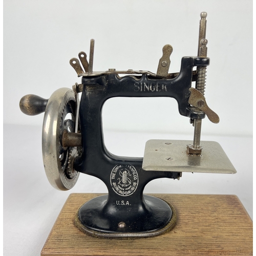 140 - An antique black cast iron toy Singer sewing machine, on a wooden base. Approx. 21cm tall.