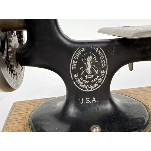 140 - An antique black cast iron toy Singer sewing machine, on a wooden base. Approx. 21cm tall.